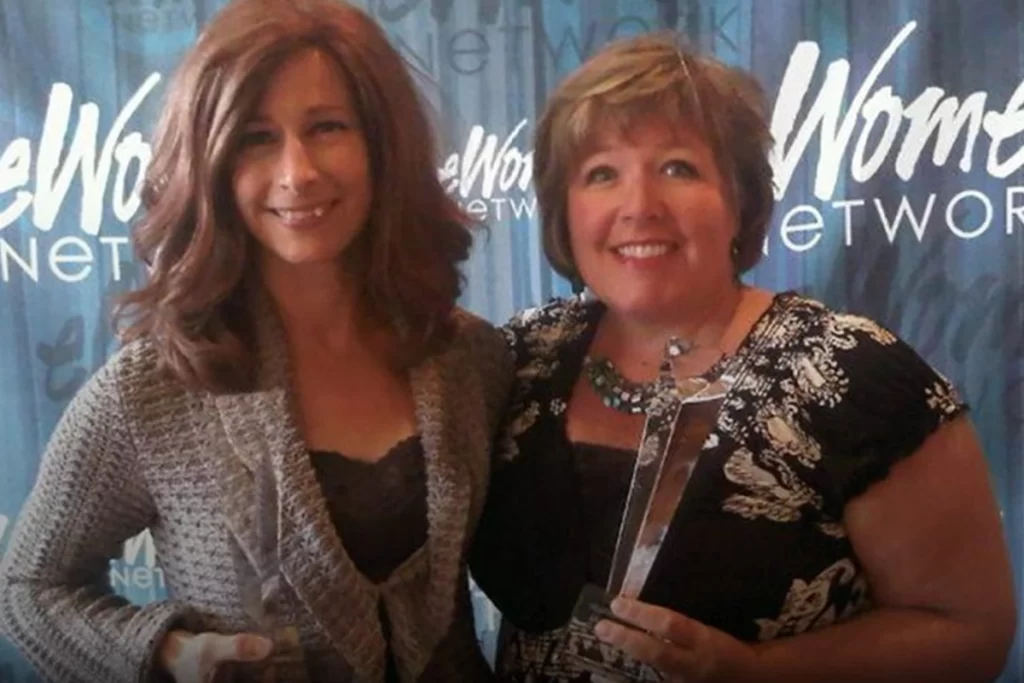 Angela Armstrong and anoter person smile at the camera while holding an award.