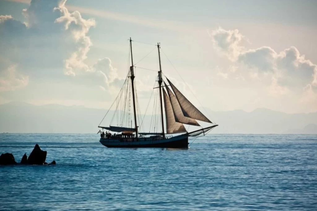 A boat with large sails sits on a calm ocean.