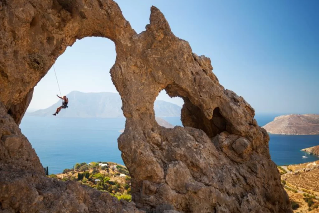 A rock climber swings between a large rock arch.
