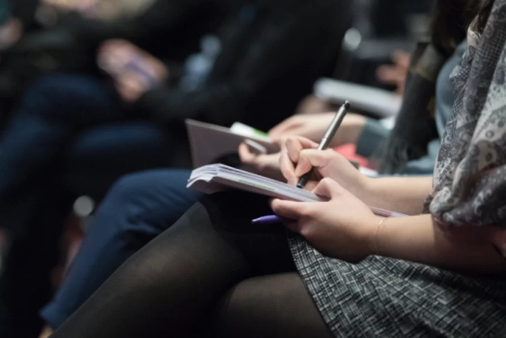 People sit in a lecture taking notes on their notepads.