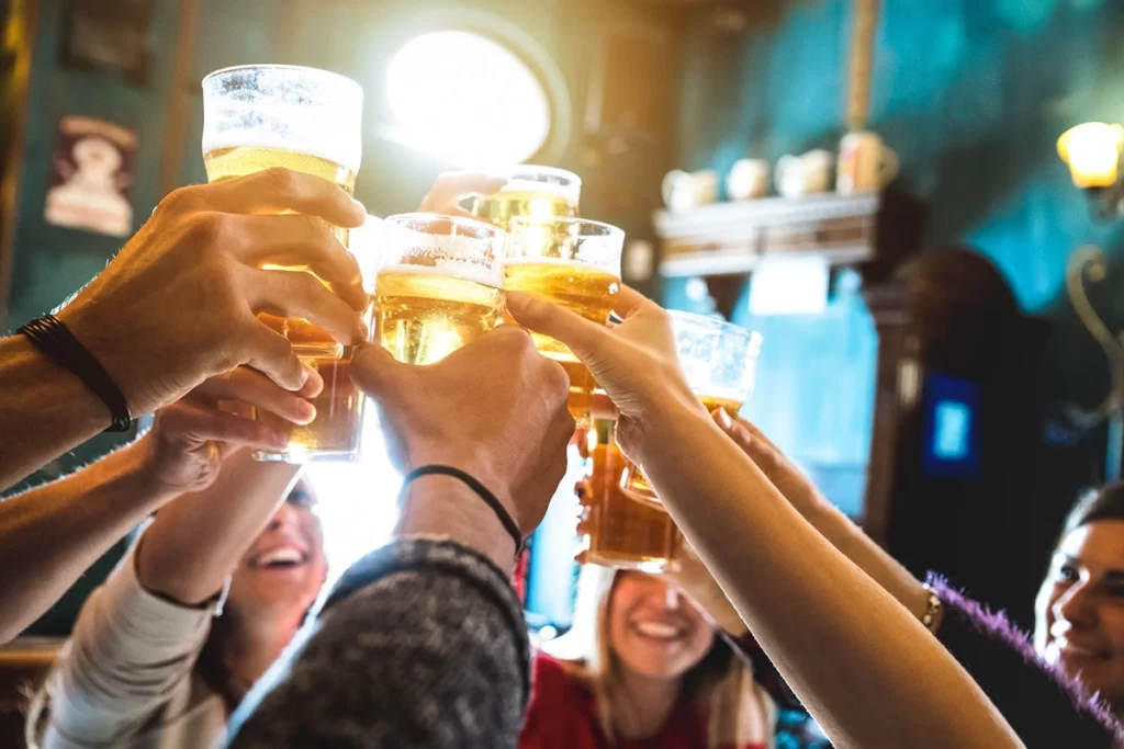 A group of people hold up glasses of beer and cheers one another.