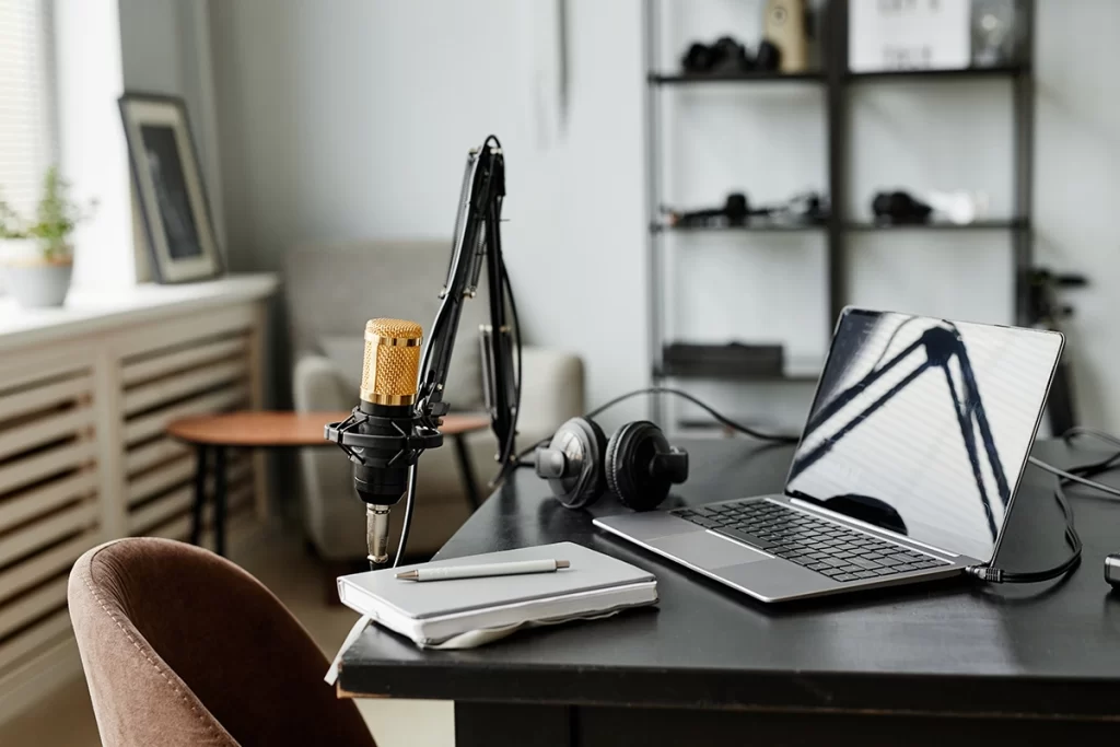 A desk with microphone, laptop, headphones, notepad, and pen.