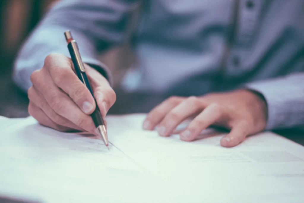 A hand holding a pen writes on a piece of paper.