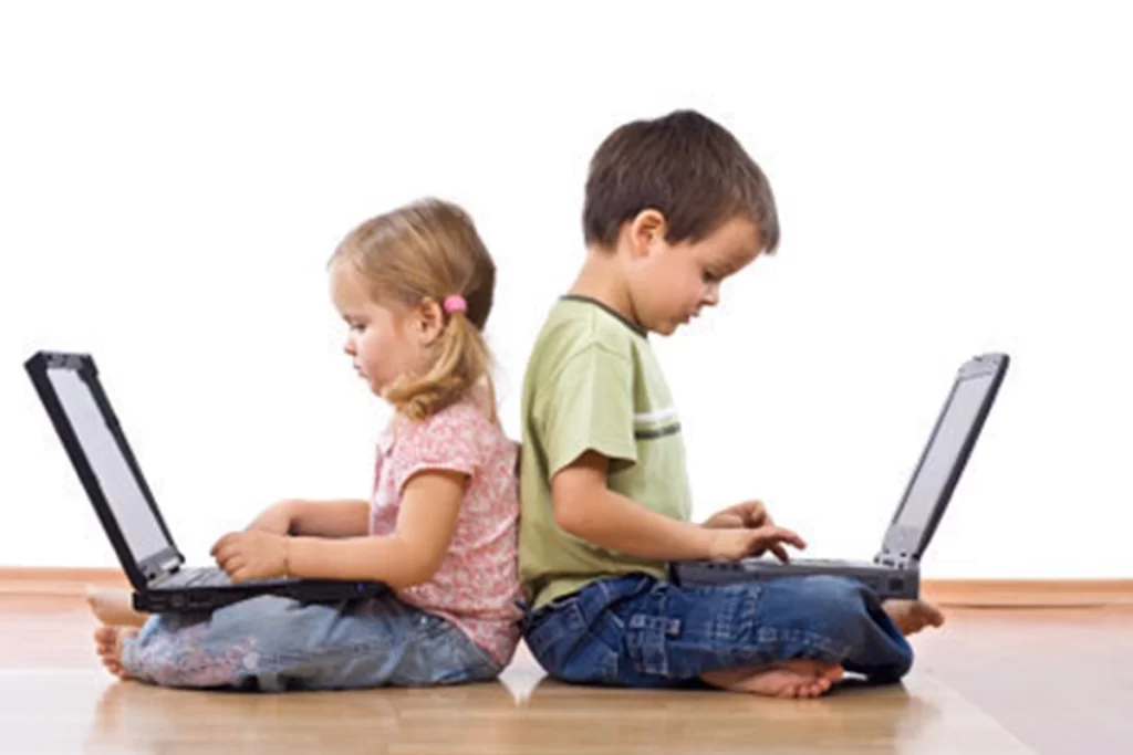 Two children sit back to back, each playing on a laptop.