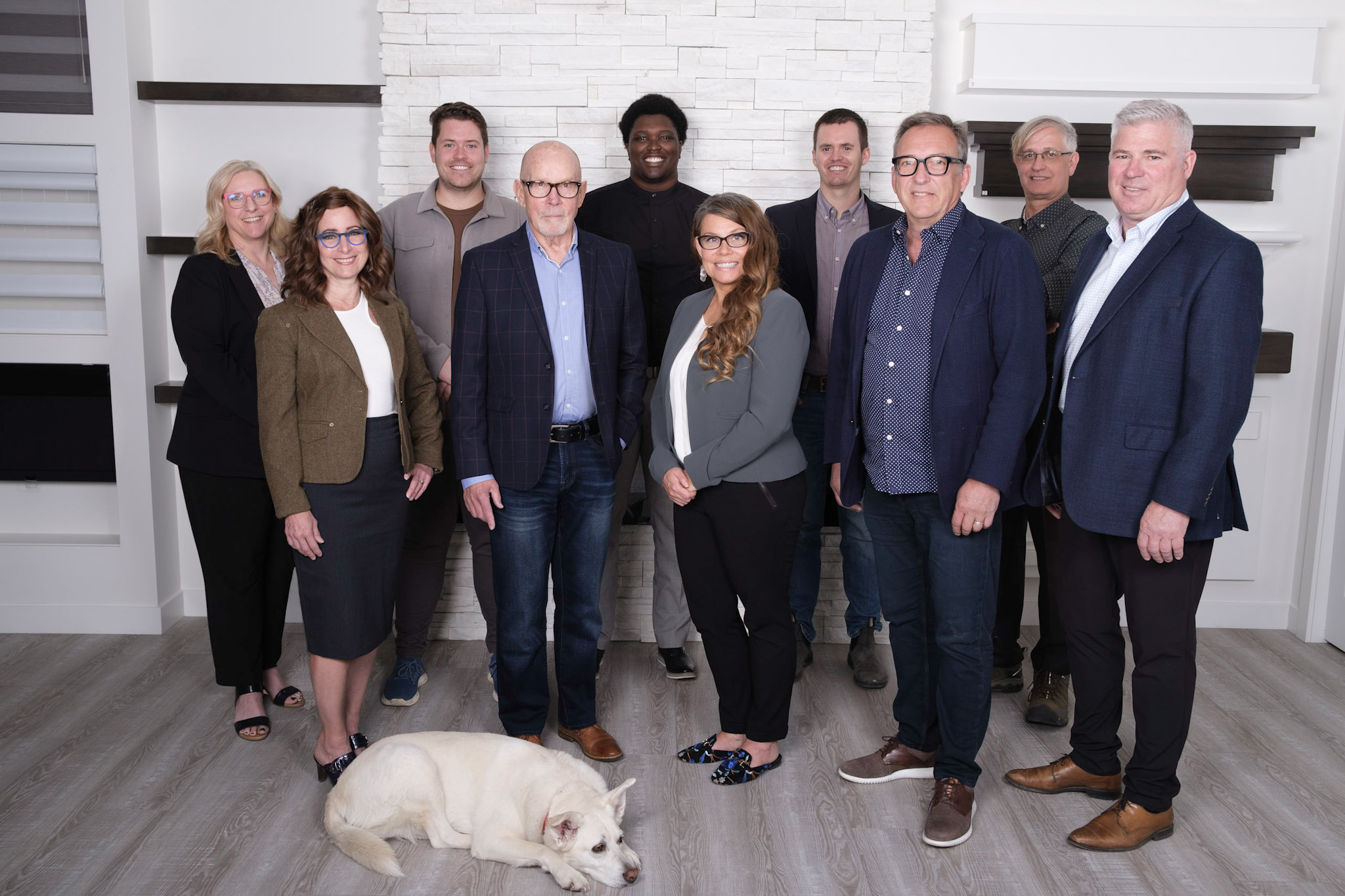 The team at Prime Capital stands in front of a white wall, smiling at the camera. A small white dog lays on the floor in front of them.